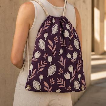 Person wearing a purple drawstring backpack printed with a cream floral and leaf pattern.